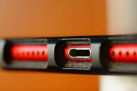 Cell phone - charging jack and speakers. Red, used phone in protective packaging. Electronics in close up.の写真素材