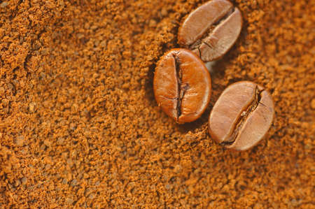 Three coffee beans on a brown background. Coffee beans on ground coffee. Macro magnification of coffee beans in daylight.の写真素材