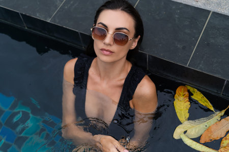 Beautiful european woman in black swimsuit posing outside at villa in swimming pool, on vacation,...