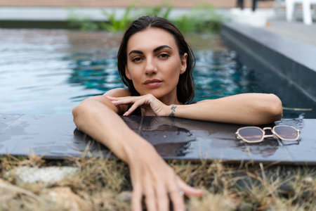 Beautiful european woman in black swimsuit posing outside at villa in swimming pool, on vacation, perfect shape, good body, tanned, fit, wearing trendy brown sunglassesの写真素材