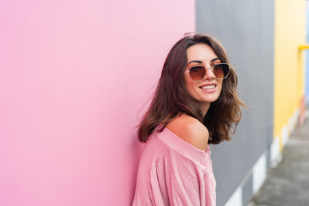 Young beautiful smiling cute romantic woman in trendy summer dress. Carefree woman posing in the street near pink wall. Positive model outdoors in sunglasses. Cheerful and happy.の写真素材
