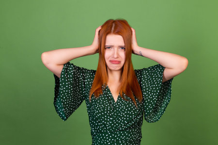 Young red hair woman on green background sad angry screaming crying