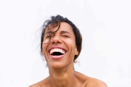 Beauty portrait of young topless african american woman with bare shoulders on white background with perfect skin and natural makeup positive laughingの写真素材
