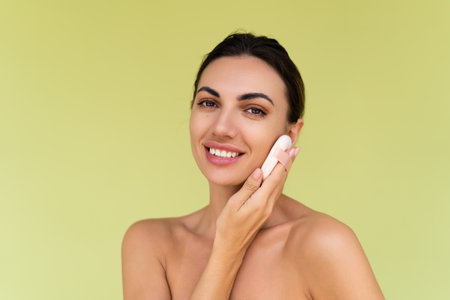 Beauty portrait of young woman with bare shoulders on green background with cosmetic powder puff velour makeup foundation blender sponge applicatorの写真素材