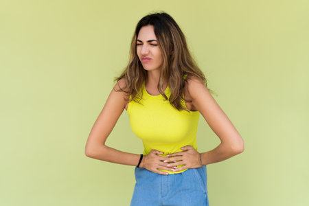 Woman wearing casual sweater on background suffering stomach ache with painful grimace, feeling sudden period cramps, gynecology concept.の写真素材