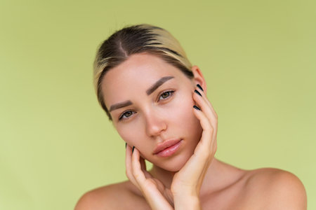 Beauty portrait of young topless woman with bare shoulders on green background with perfect skin and natural makeupの写真素材