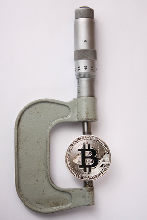 the bitcoin is measured with a micrometer on a white backgroundの写真素材