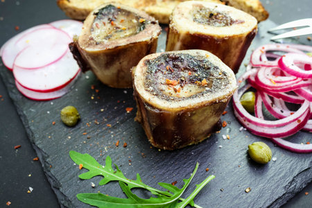 close up of rustic english bone marrow, pickled onion and toast on a basalt plate
