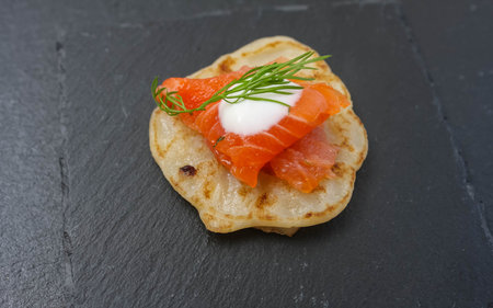 Salted salmon with dill on a pancake. Black basalt plate.