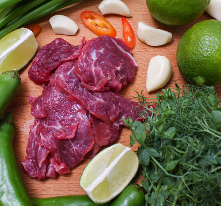 Raw beef sliced on a board with fresh vegetables. The view from the top