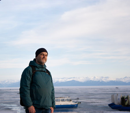 Portrait of a man in winter clothes against the background of the frozen Lake Baikal. Mountains....