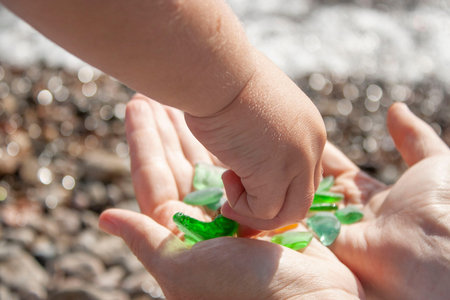 Pick up garbage shards of glass along the beach and collect them in hand. the child helps his mother...