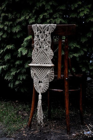 Macrame handmade on a wooden chair in the garden. Background of fir branches, thujaの写真素材