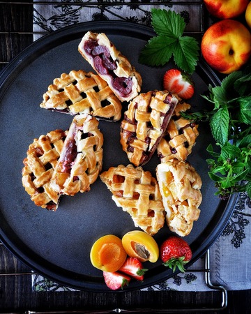 Patties with a lattice made of dough. Stuffing from strawberries, apricots, nectarines, peaches, cherries. On a grill. On a metal dishの写真素材