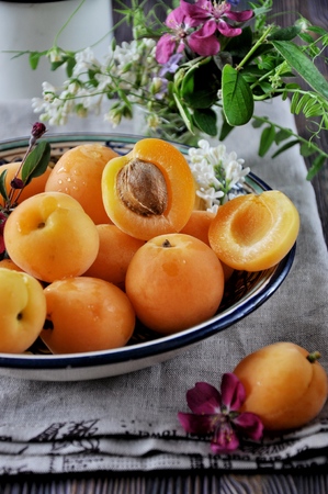 On a wooden table on a platter of fresh apricots with bones, decorated with flowersの写真素材