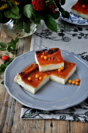 On the wooden plate is a curd cake with a sea-buckthorn. Decorated with flowers and a branch with hipsの写真素材