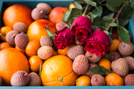 Gift set for the girl. A box of fresh fruit with red oranges, mini tangerines, lychee fruits and red rosesの写真素材
