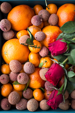 Gift set for the girl. A box of fresh fruit with red oranges, mini tangerines, lychee fruits and red rosesの写真素材