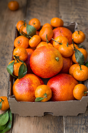 A cardboard box of fresh winter fruits with red oranges and mini tangerines. On a wooden backgroundの写真素材