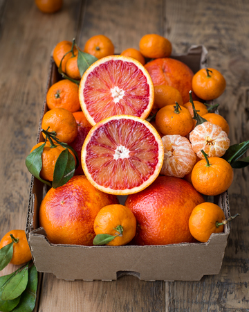 A cardboard box of fresh winter fruits with red oranges and mini tangerines. On a wooden backgroundの写真素材