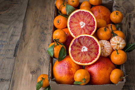 A cardboard box of fresh winter fruits with red oranges and mini tangerines. On a wooden backgroundの写真素材