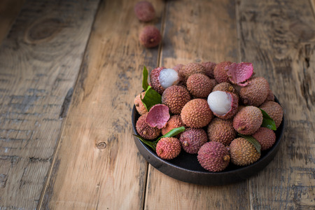 Still life of fresh lychee fruits in a black plate on a wooden background. Rustic styleの写真素材