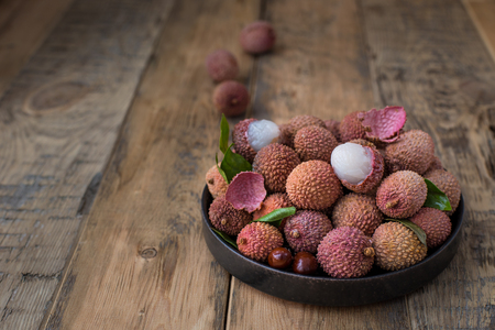 Still life of fresh lychee fruits in a black plate on a wooden background. Rustic styleの写真素材