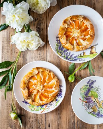Homemade open apricot pie (shortcrust pastry with apricot filling, peonies in the background). On a wooden kitchen tableの写真素材