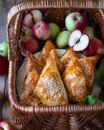 Homemade triangular pies with apples from ready-made puff pastry, in a wooden wicker basket, with fresh applesの写真素材