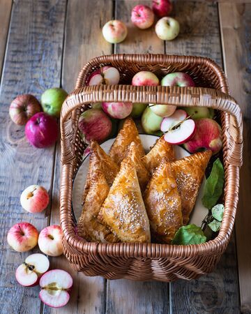 Homemade triangular pies with apples from ready-made puff pastry, in a wooden wicker basket, with fresh applesの写真素材