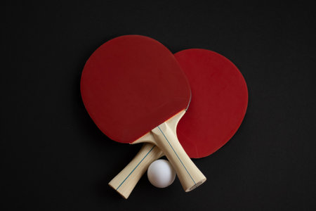Two red table tennis paddles and a white ball arranged on a black background. High quality photoの写真素材