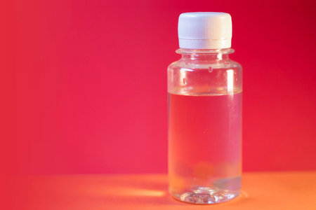 Clear plastic bottle with liquid on vibrant red and orange background. High quality photoの写真素材