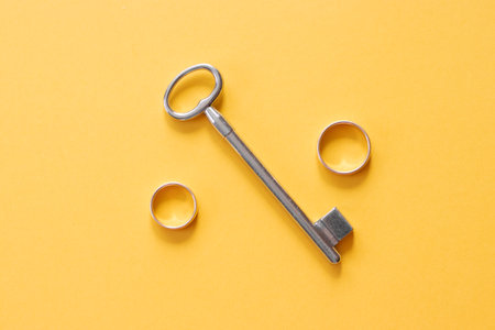 Gold wedding rings and old key on yellow backgroundの写真素材