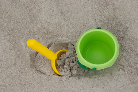 Green bucket and yellow shovel lying on sand at the beachの写真素材