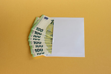 White envelope filled with 100 euro banknotes on a bright yellow background.