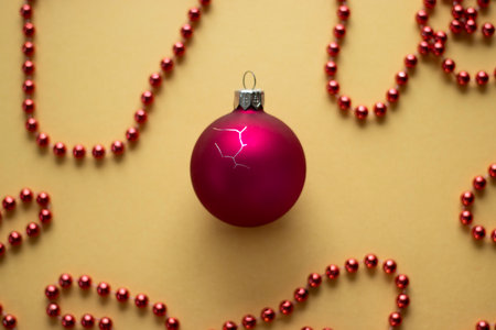 Cracked red Christmas bauble with red bead garlands on yellow background. High quality photoの写真素材