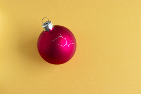Cracked red Christmas ornament on yellow backgroundの写真素材