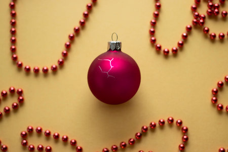 Cracked red Christmas bauble with red bead garlands on yellow background