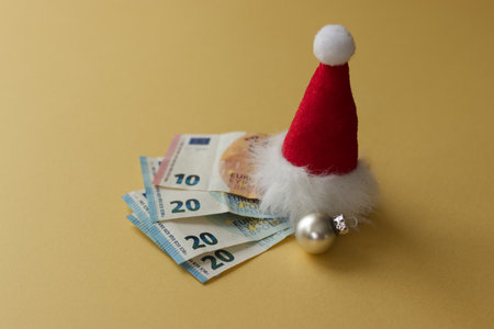 Euro money and Christmas bauble with Santa hat on yellow background. High quality photoの写真素材