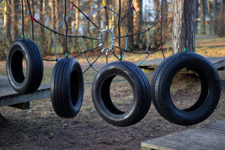 Children playground obstacle with hanging tires in forest