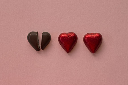Broken dark chocolate heart and two red hearts placed side by sideの写真素材