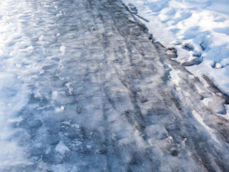 Extremely slippery footpath covered with melting snow and visible frozen ice footprints after heavy snowing in park in winter. Danger of falling and injuryの写真素材