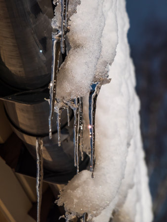Macro shot of icicles hanging from rooftop from melting snow covering a lot of snow. Winter sceneryの写真素材