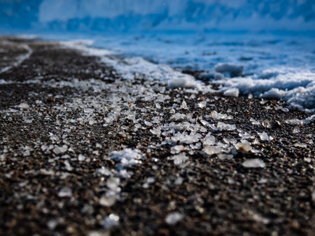 Macro shot of salt grains on icy sidewalk surface in the winter. Applying salt to keep roads clear and people safe in winter weather from ice or snow, closeup viewの写真素材