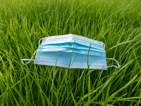 Medical mask in fresh, green spring grass. Concept of face mask as a symbol of COVID-19 pandemic in...