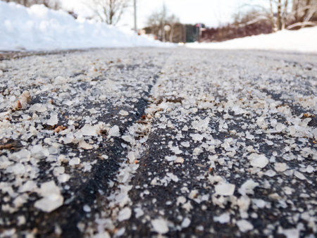 Macro shot of salt grains on icy sidewalk surface in the winter. Applying salt to keep roads clear...