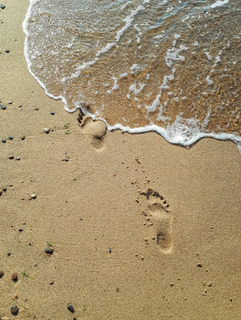 Human footprints in yellow beach sand from walking barefoot near the Baltic sea shore with water...
