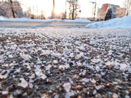 Salt grains on icy sidewalk surface in the winter. Applying salt to keep road clear and people safe in winter weather from ice or snow. Macro view of salt grains with winter scenery in bacgroundの写真素材