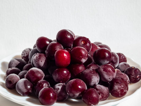 Frozen sweet, ripe cherry berries covered with white and melting hoarfrost on white plate with white...