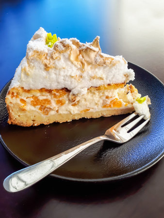 Triangular piece of dessert cake with cream, cottage cheese and pieces of peaches, meringue and...